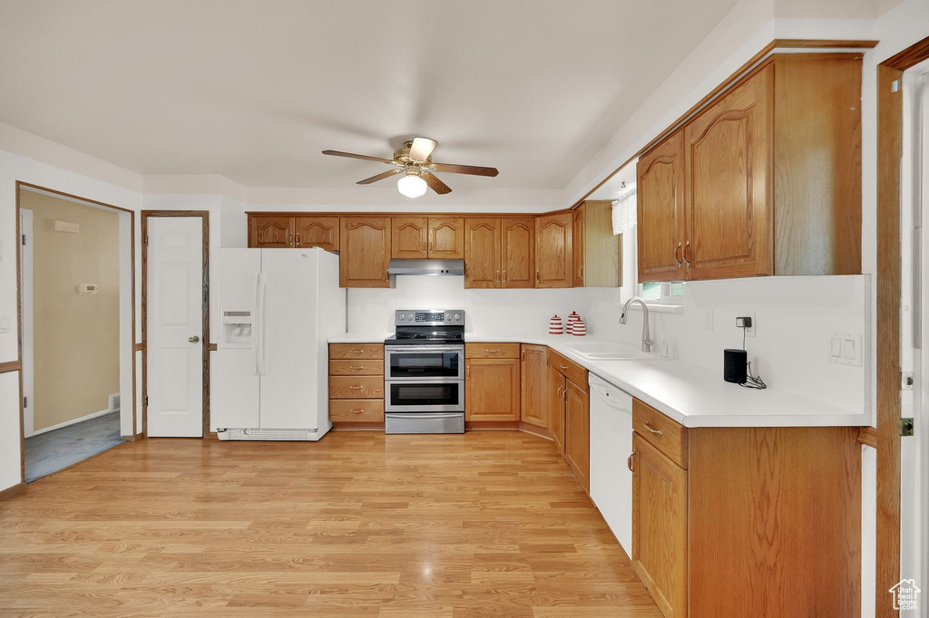 Kitchen featuring white appliances, under cabinet range hood, a ceiling fan, light wood-style floors, and brown cabinetry