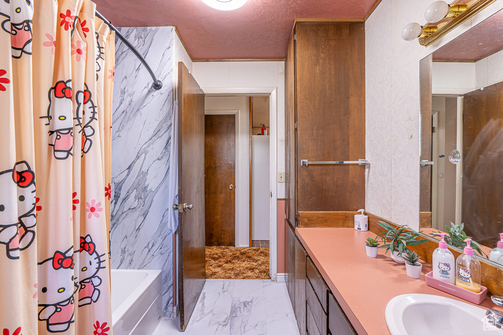 Full bathroom featuring marble look tiles, vanity, shower / bath combo with shower curtain, and a textured ceiling