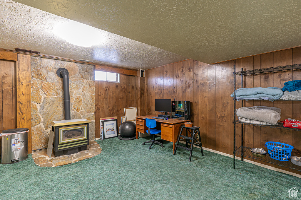 Office area with a textured ceiling, carpet flooring, a wood stove, and wooden walls