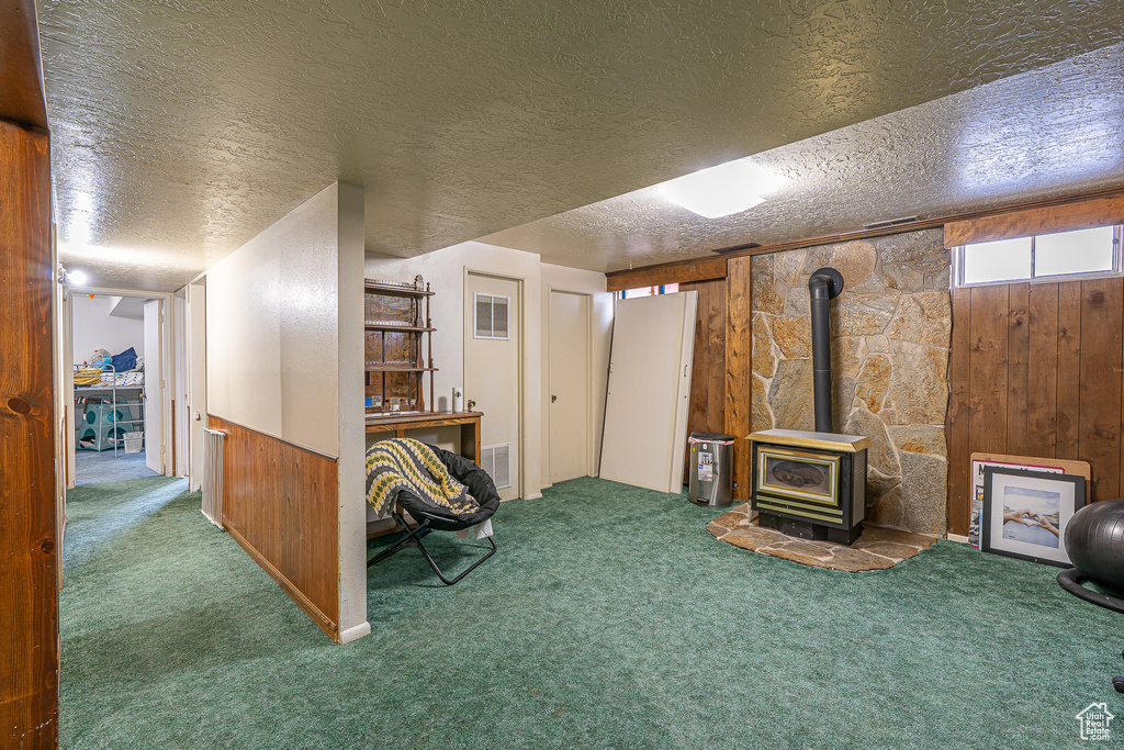 Below grade area featuring carpet flooring, a wood stove, wood walls, and a textured ceiling