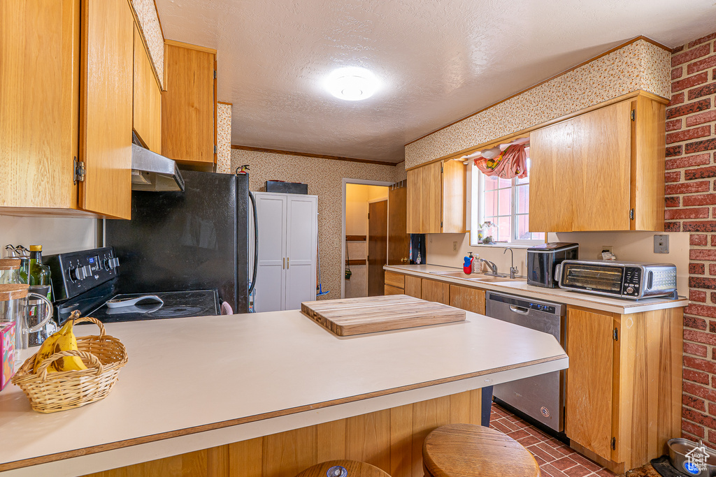 Kitchen with black appliances, light countertops, under cabinet range hood, a peninsula, and brick wall