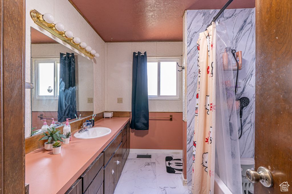 Bathroom with vanity, marble finish floors, plenty of natural light, shower / bathtub combination with curtain, and a textured ceiling