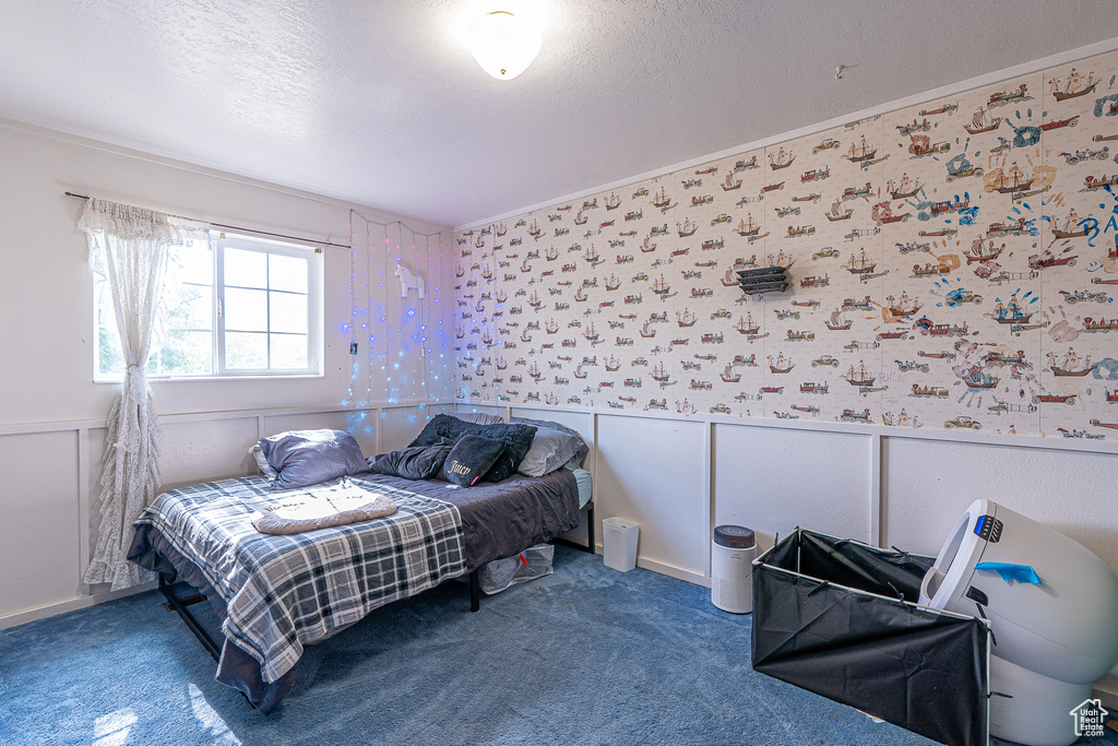 Bedroom with a wainscoted wall, carpet, wallpapered walls, and a textured ceiling