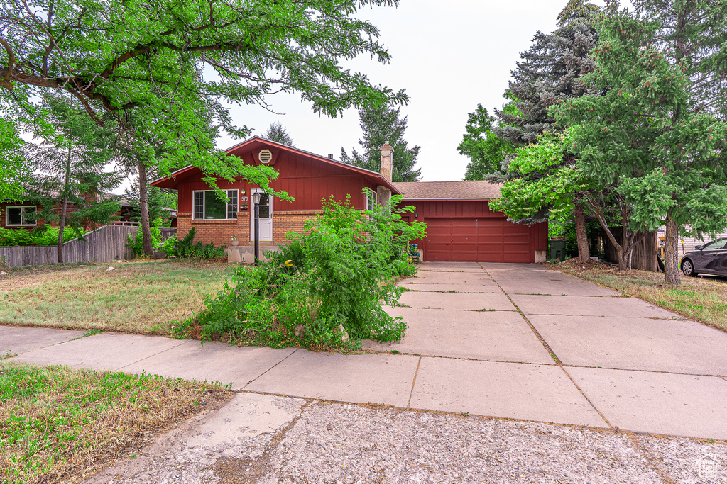 View of front facade featuring an attached garage, concrete driveway, brick siding, and a chimney