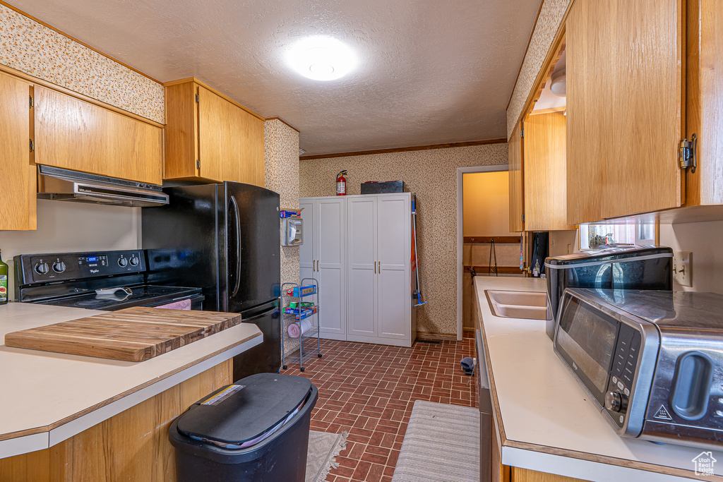 Kitchen featuring exhaust hood, black appliances, brick patterned floors, light countertops, and a textured ceiling