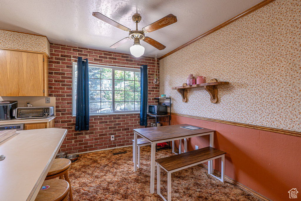 Home office featuring a ceiling fan, crown molding, a wainscoted wall, brick wall, and a wood stove