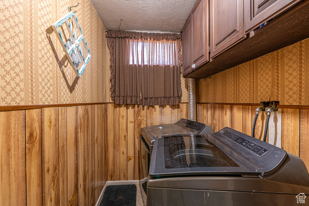 Laundry area featuring washer and clothes dryer, cabinet space, a textured ceiling, and wallpapered walls