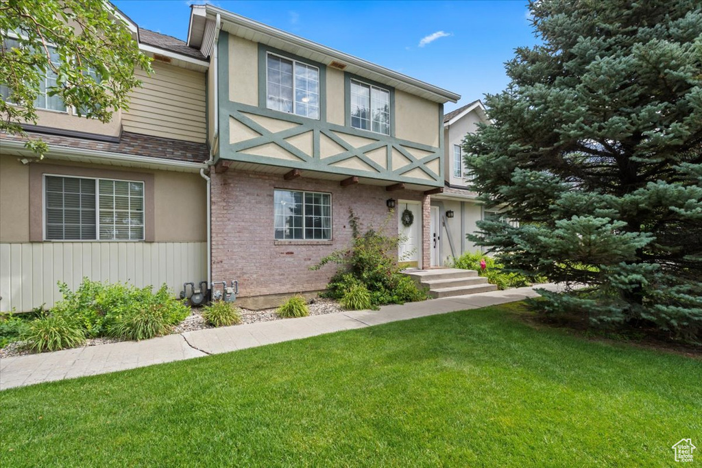 View of front of house with a front yard, stucco siding, brick siding, and a shingled roof