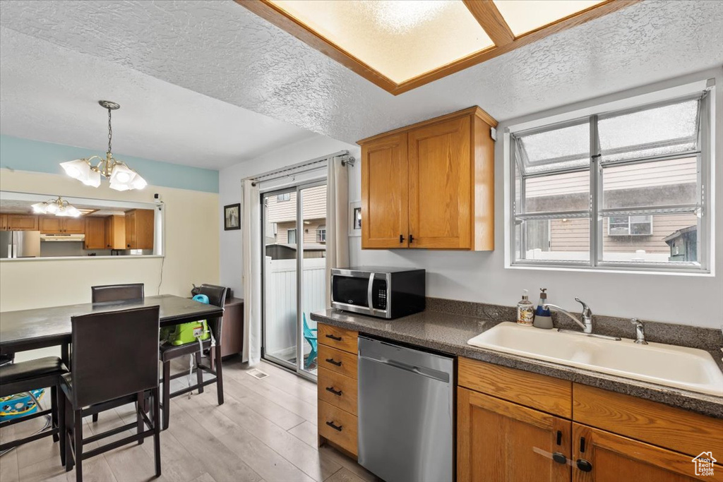 Kitchen with stainless steel appliances, healthy amount of natural light, under cabinet range hood, a chandelier, and a textured ceiling