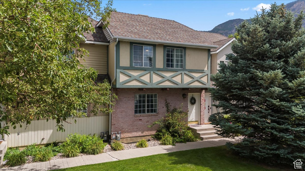 View of front of property featuring brick siding, a mountain view, a shingled roof, a front yard, and stucco siding