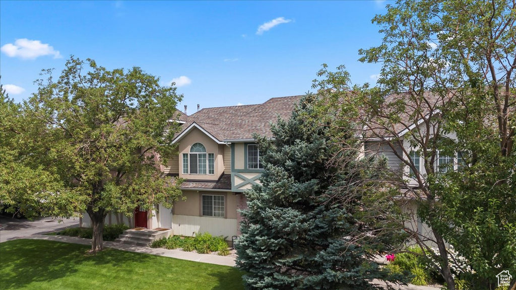 View of front of property with a front lawn, stucco siding, and a shingled roof