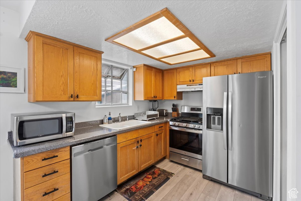 Kitchen with stainless steel appliances, light wood-style floors, under cabinet range hood, dark countertops, and a textured ceiling