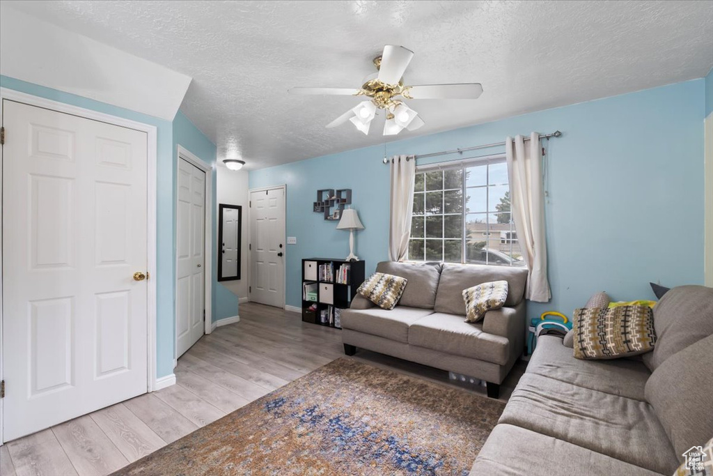 Living area with light wood-style floors, a ceiling fan, and a textured ceiling