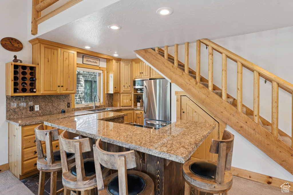 Kitchen with stainless steel appliances, a kitchen breakfast bar, tasteful backsplash, recessed lighting, and light stone counters