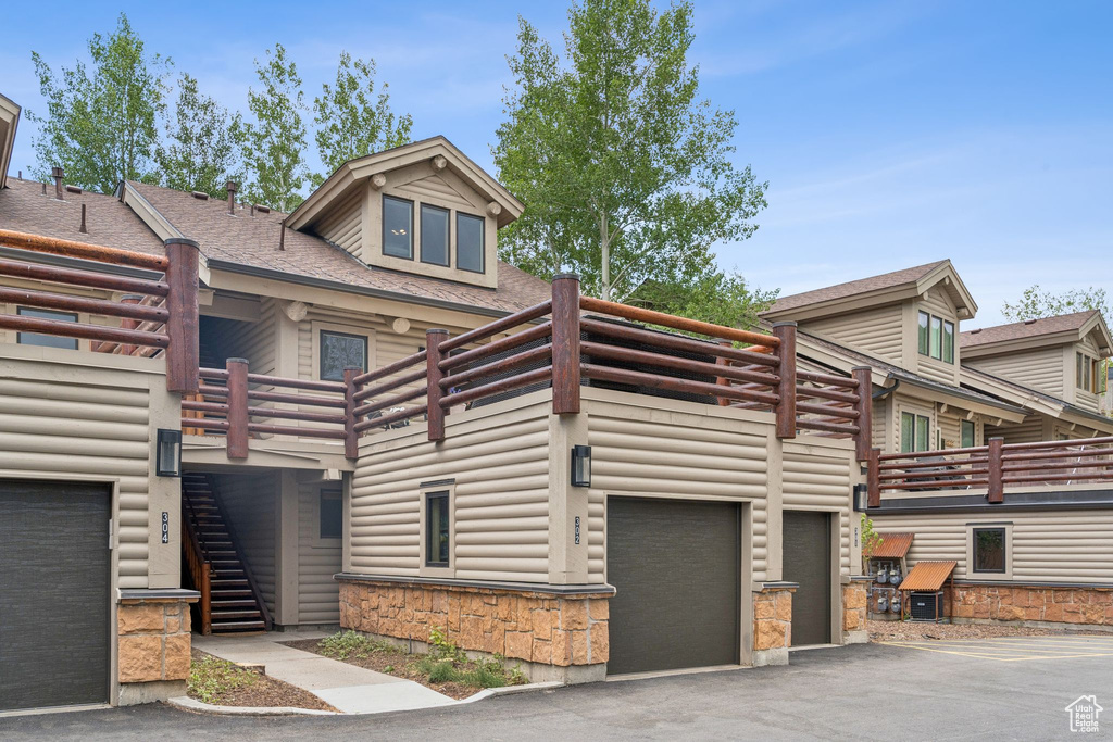 View of front of property with stairs, an attached garage, driveway, and stone siding
