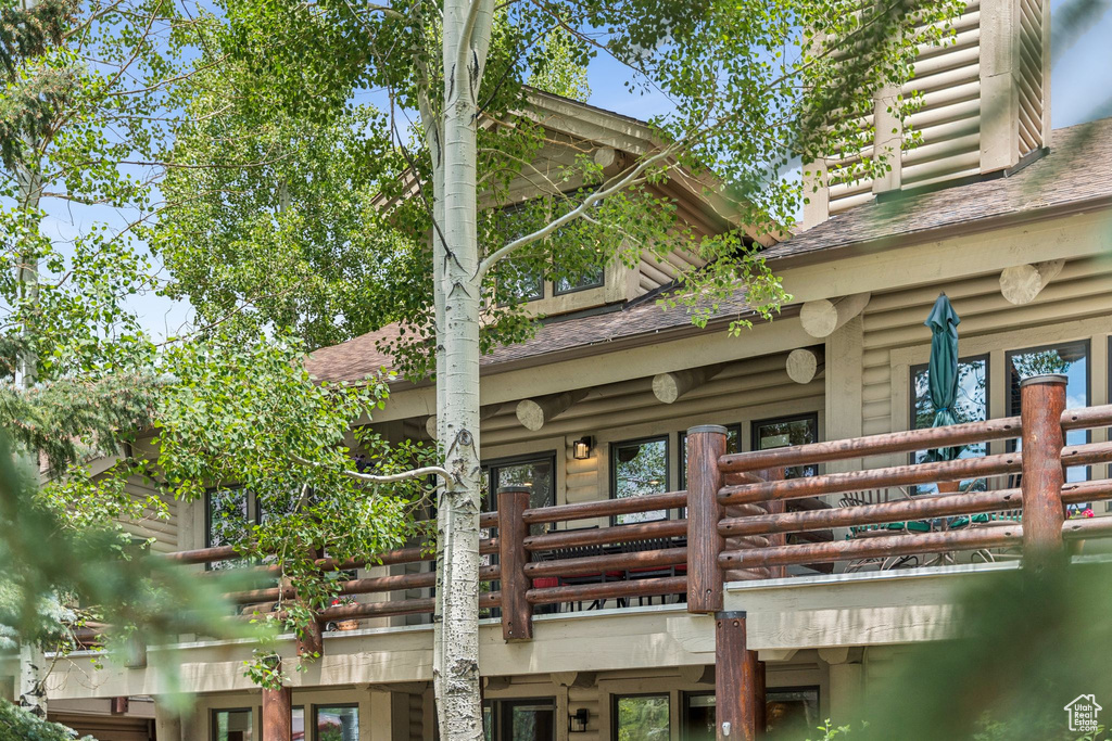 Rear view of house featuring a shingled roof, log siding, and a balcony