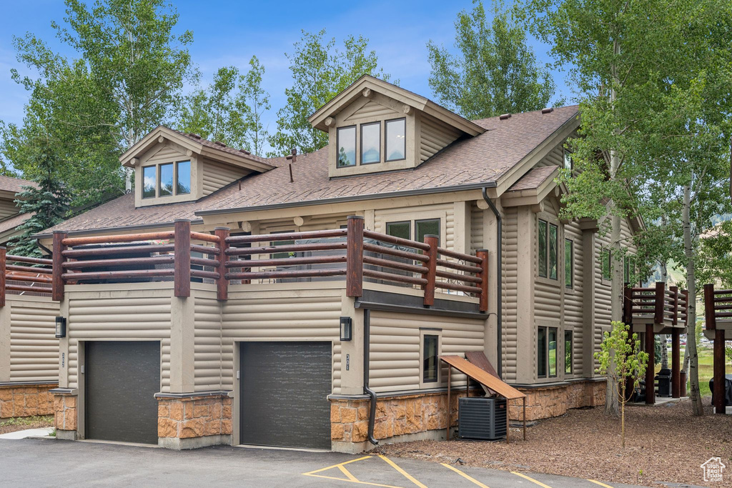View of front of home featuring a balcony, an attached garage, a shingled roof, and asphalt driveway