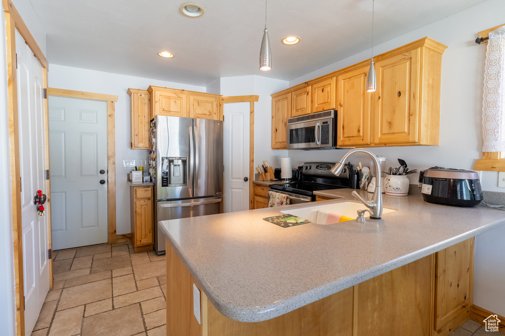 Kitchen featuring appliances with stainless steel finishes, a peninsula, recessed lighting, decorative light fixtures, and light stone finish floors