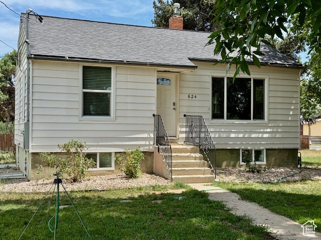 View of front of property featuring a chimney, a front lawn, and a shingled roof