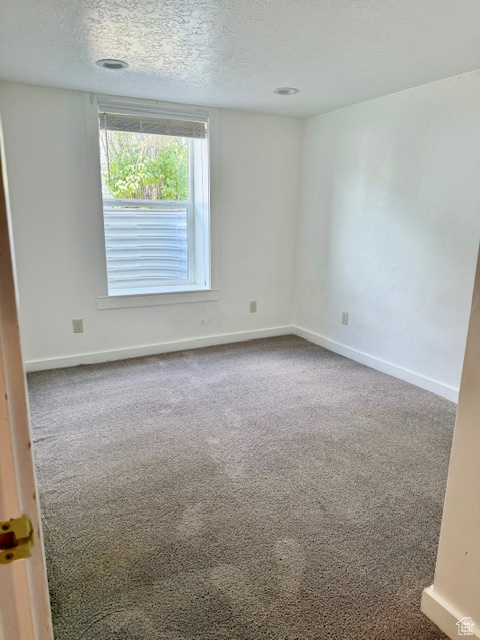 Carpeted spare room with a textured ceiling and baseboards