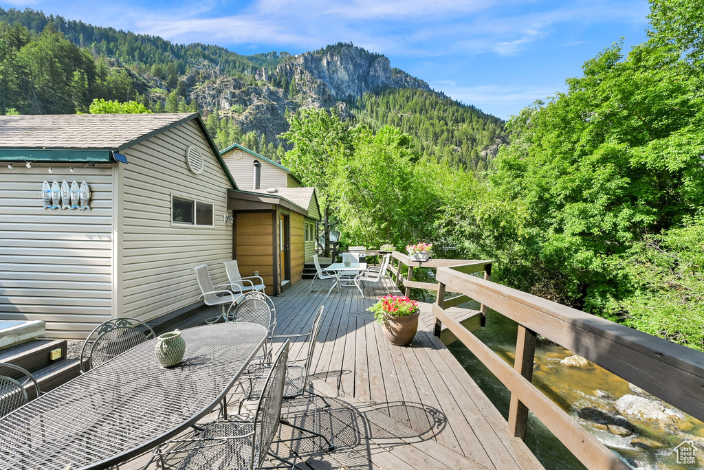 Wooden deck featuring outdoor dining space, a forest view, and a mountain view