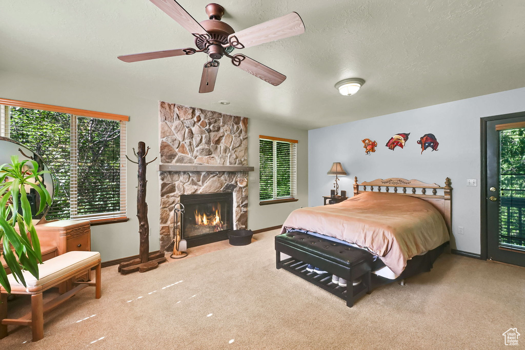 Bedroom with carpet floors, multiple windows, access to outside, and a stone fireplace