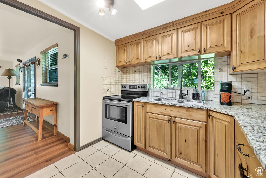 Kitchen with stainless steel electric stove, tasteful backsplash, light stone counters, and light wood-style flooring