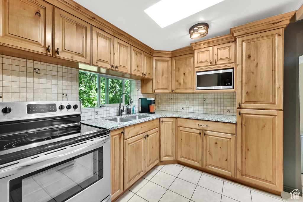 Kitchen featuring appliances with stainless steel finishes, light tile patterned floors, light stone countertops, and decorative backsplash
