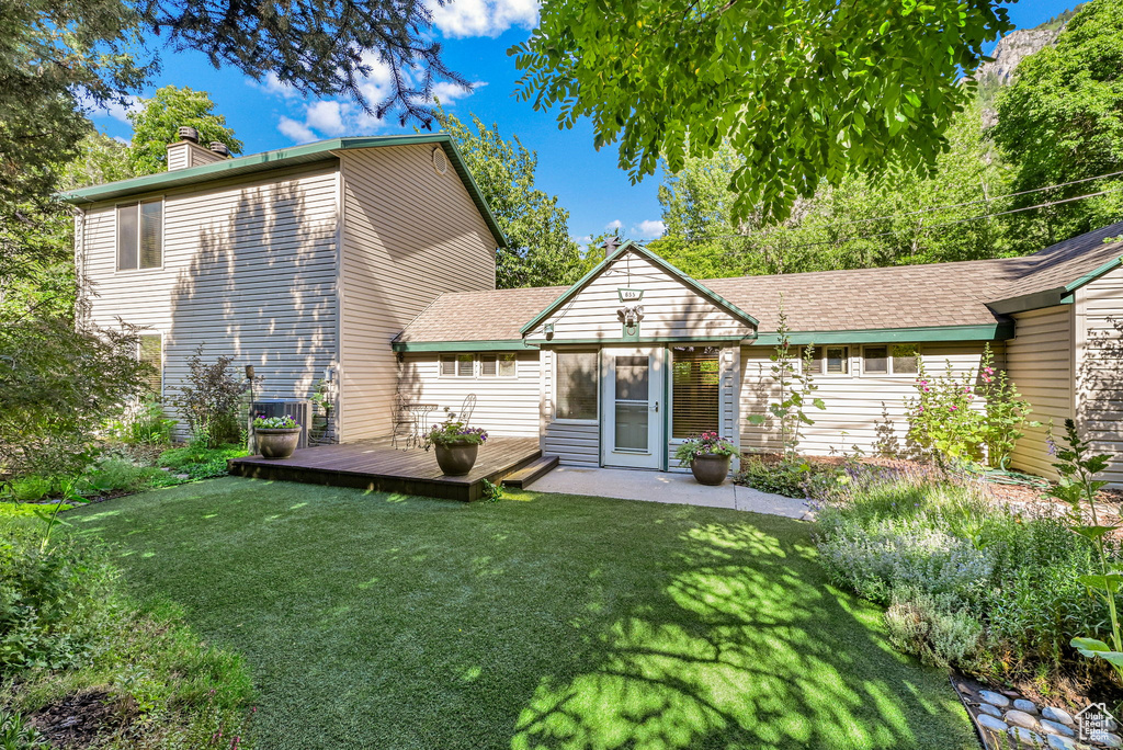 Rear view of property featuring a chimney, a deck, and a yard