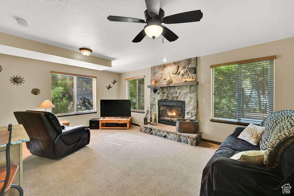 Carpeted living area featuring a fireplace and a ceiling fan