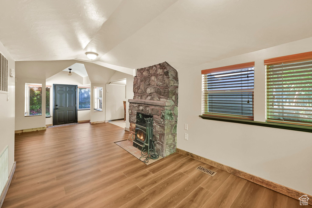 Unfurnished living room with wood finished floors, lofted ceiling, and a fireplace