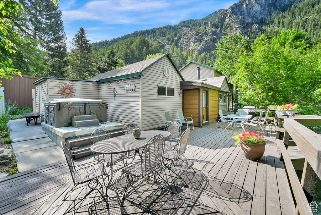 Deck with a hot tub, outdoor dining area, a view of trees, and a mountain view