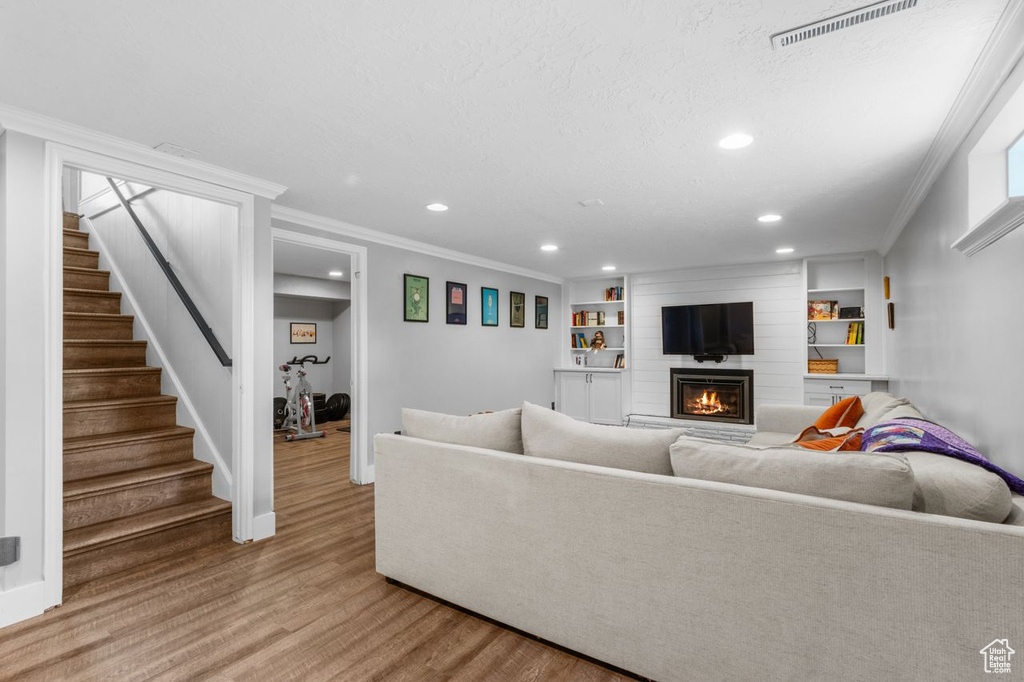 Living room featuring wood finished floors, recessed lighting, ornamental molding, a large fireplace, and stairs