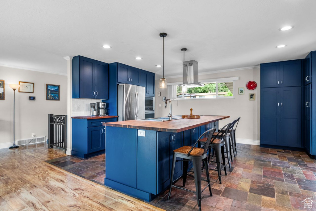 Kitchen featuring butcher block countertops, freestanding refrigerator, blue cabinetry, a breakfast bar area, and crown molding