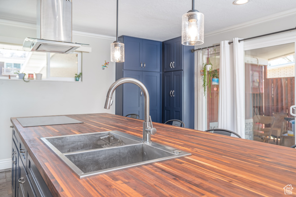Kitchen with wood counters, blue cabinets, crown molding, island range hood, and decorative light fixtures
