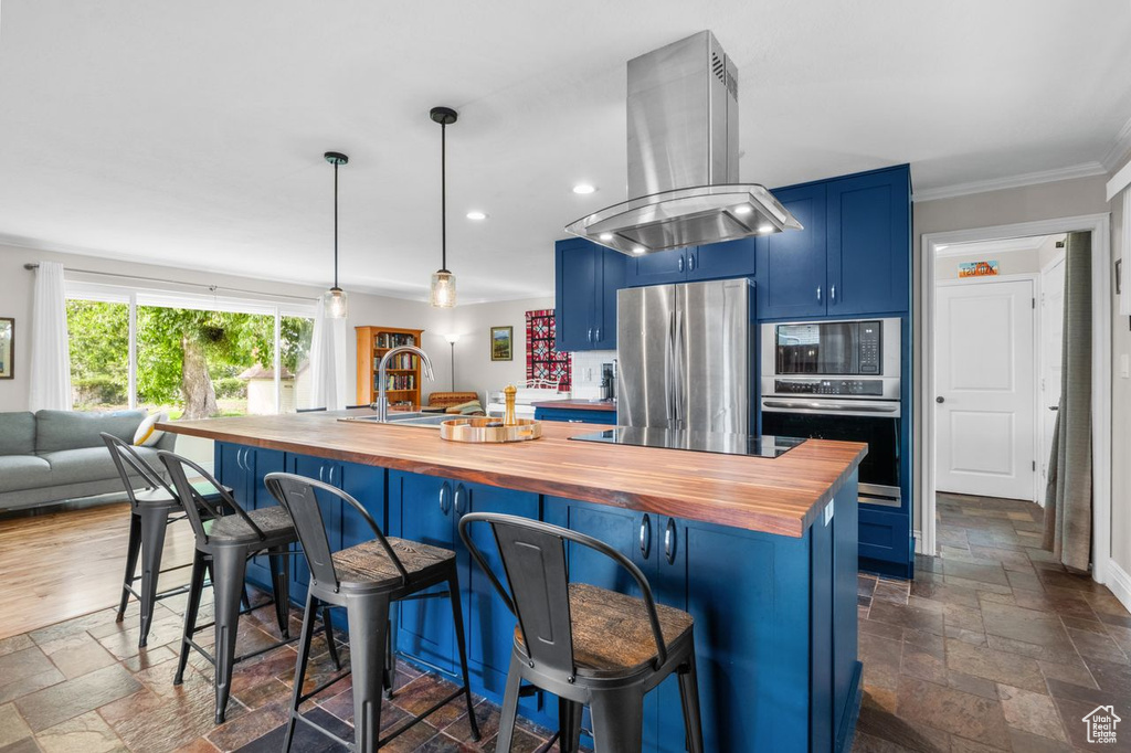 Kitchen with wooden counters, island range hood, blue cabinets, appliances with stainless steel finishes, and stone tile floors