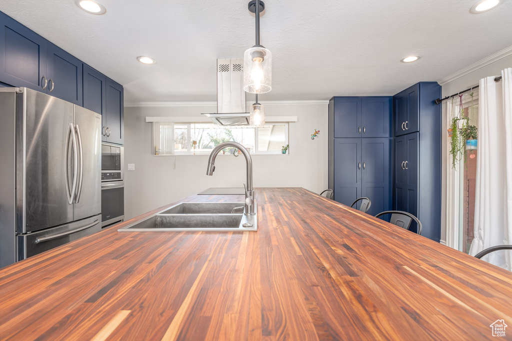Kitchen with butcher block counters, stainless steel appliances, ornamental molding, recessed lighting, and blue cabinets