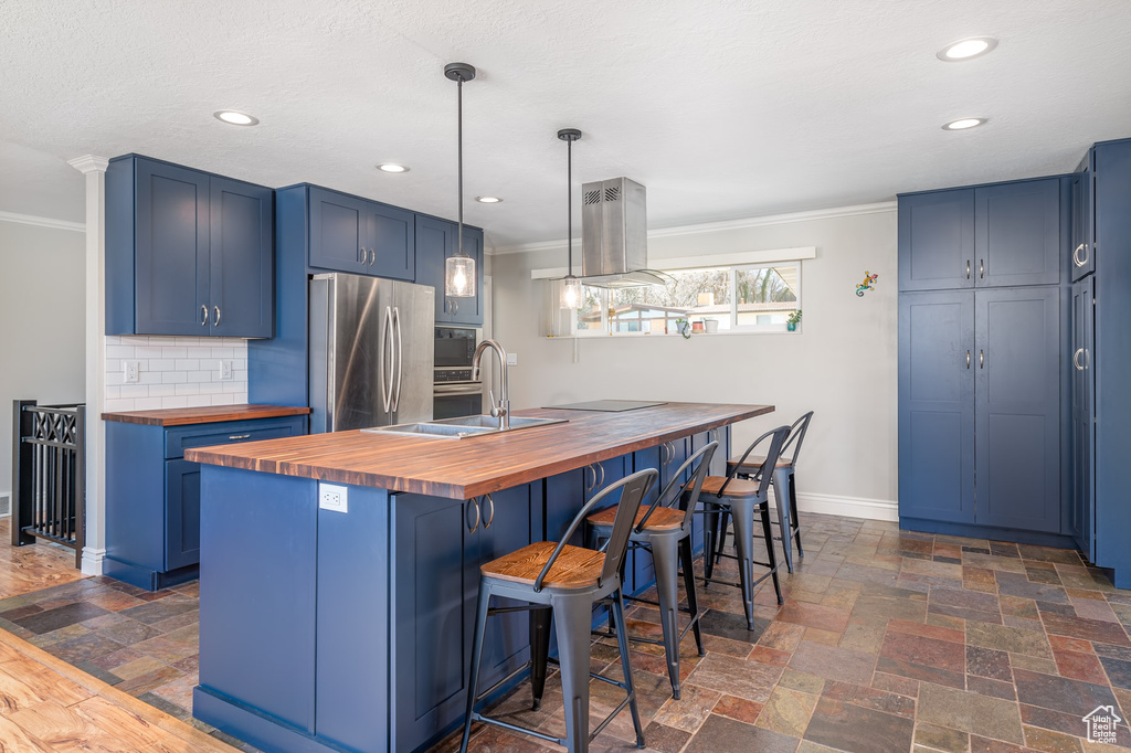 Kitchen with wooden counters, freestanding refrigerator, blue cabinetry, ornamental molding, and recessed lighting