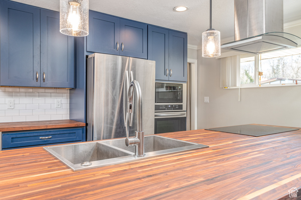 Kitchen with butcher block counters, island range hood, black appliances, blue cabinetry, and ornamental molding