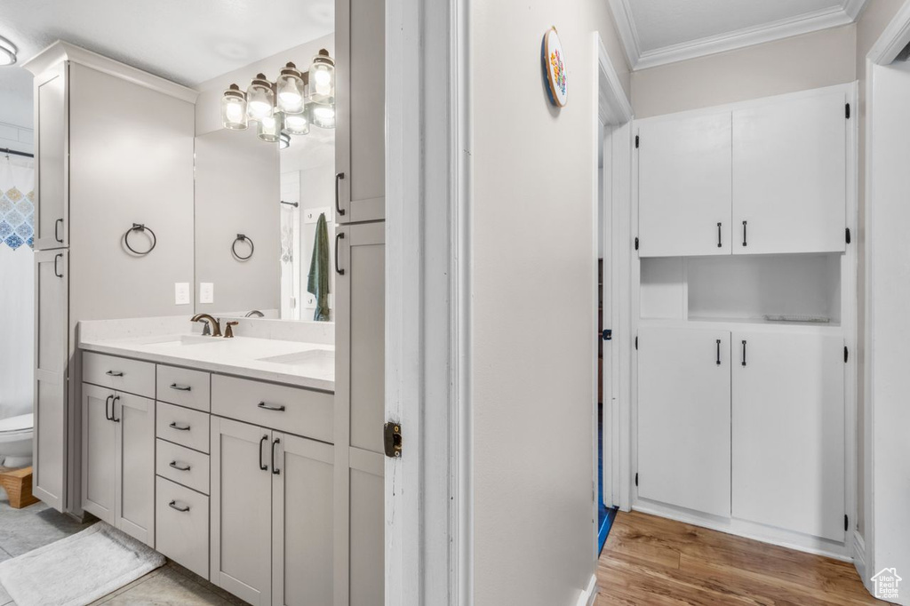 Full bath with ornamental molding, double vanity, and wood finished floors