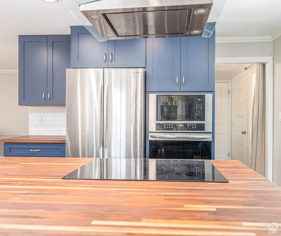 Kitchen featuring butcher block countertops, black appliances, range hood, blue cabinets, and tasteful backsplash