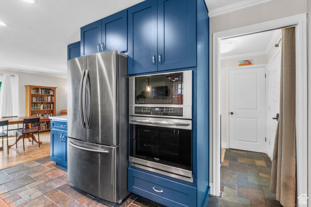 Kitchen with appliances with stainless steel finishes, blue cabinetry, crown molding, stone tile floors, and recessed lighting