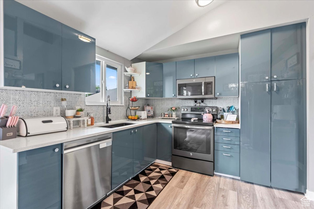 Kitchen featuring appliances with stainless steel finishes, vaulted ceiling, tasteful backsplash, light countertops, and light wood-style flooring