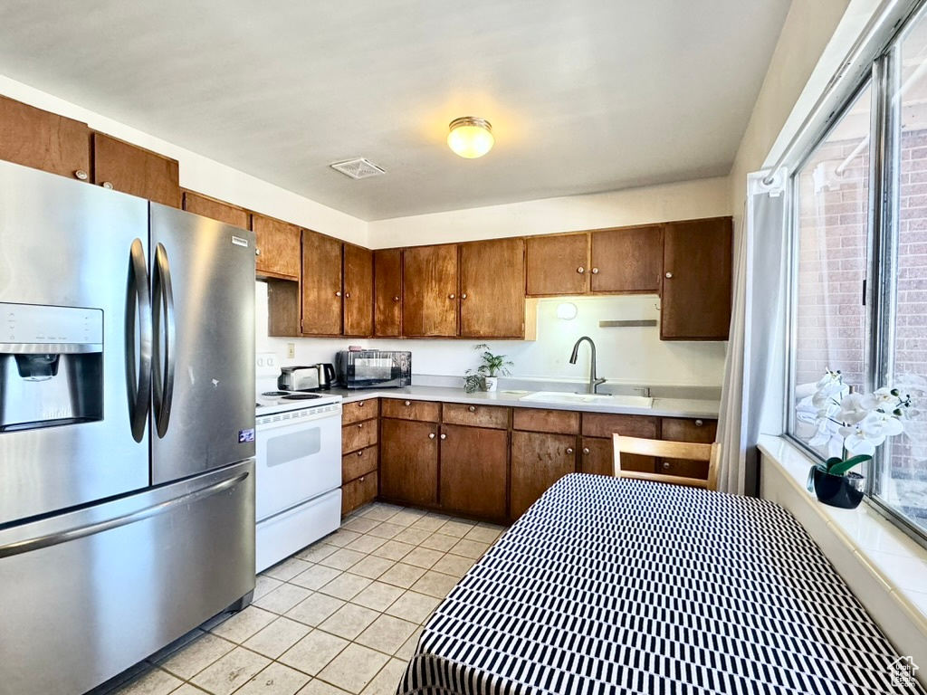 Kitchen featuring stainless steel fridge with ice dispenser, white range with electric cooktop, light countertops, light tile patterned flooring, and black microwave
