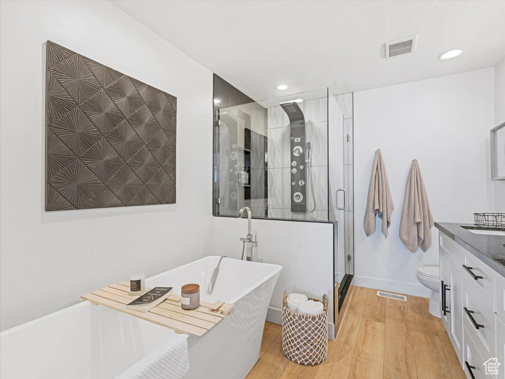 Full bathroom with vanity, wood finished floors, a shower stall, a soaking tub, and recessed lighting