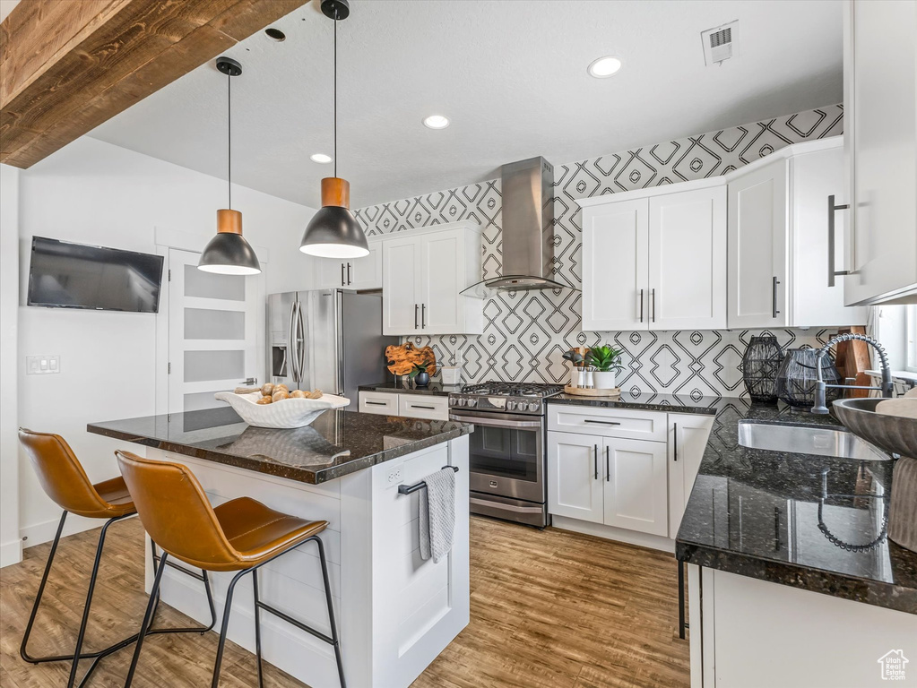Kitchen with wall chimney range hood, appliances with stainless steel finishes, white cabinetry, wood finished floors, and recessed lighting
