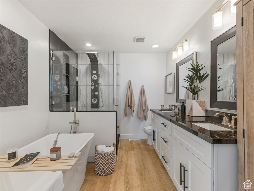 Full bath featuring a stall shower, double vanity, a soaking tub, wood finished floors, and recessed lighting