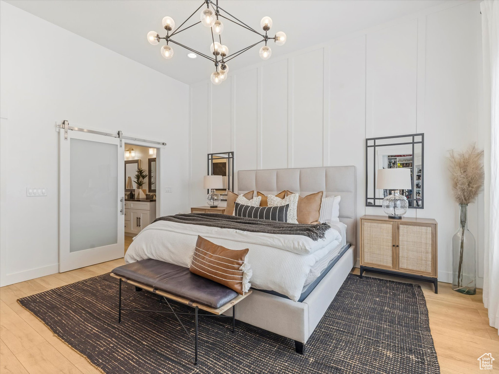 Bedroom featuring light wood finished floors, a barn door, a chandelier, and connected bathroom