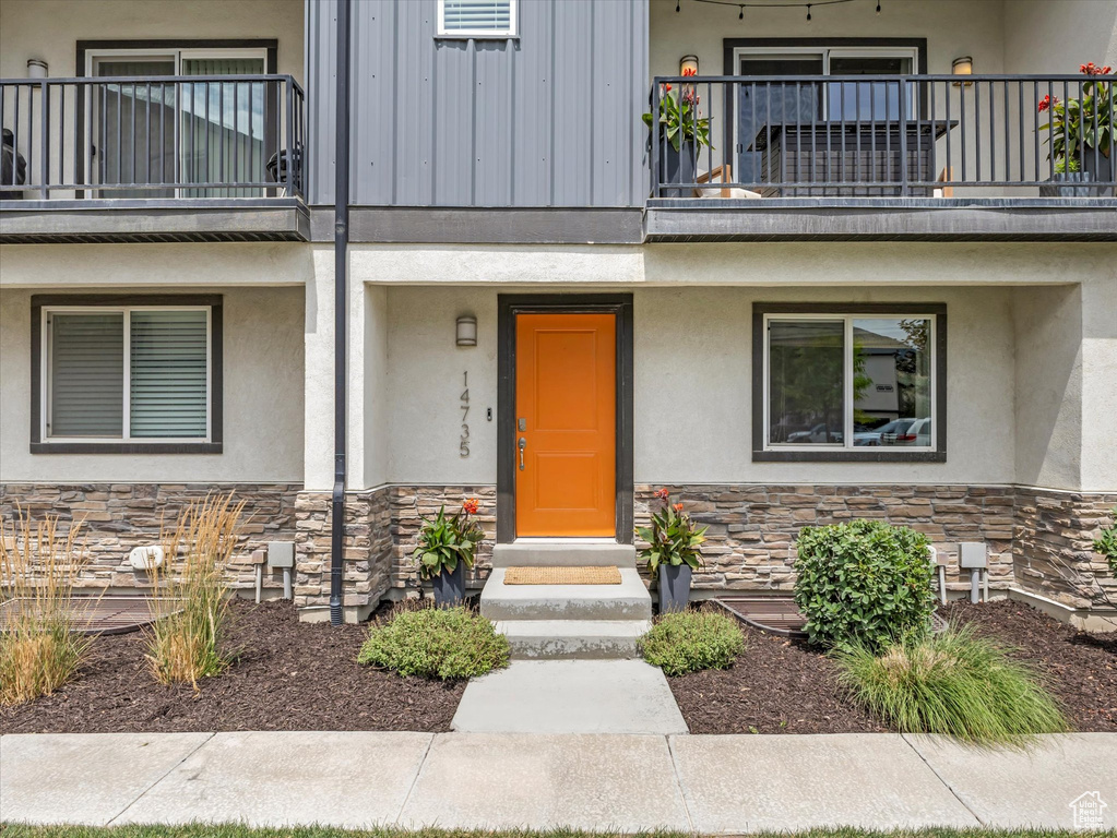 Entrance to property featuring a balcony, stone siding, and stucco siding