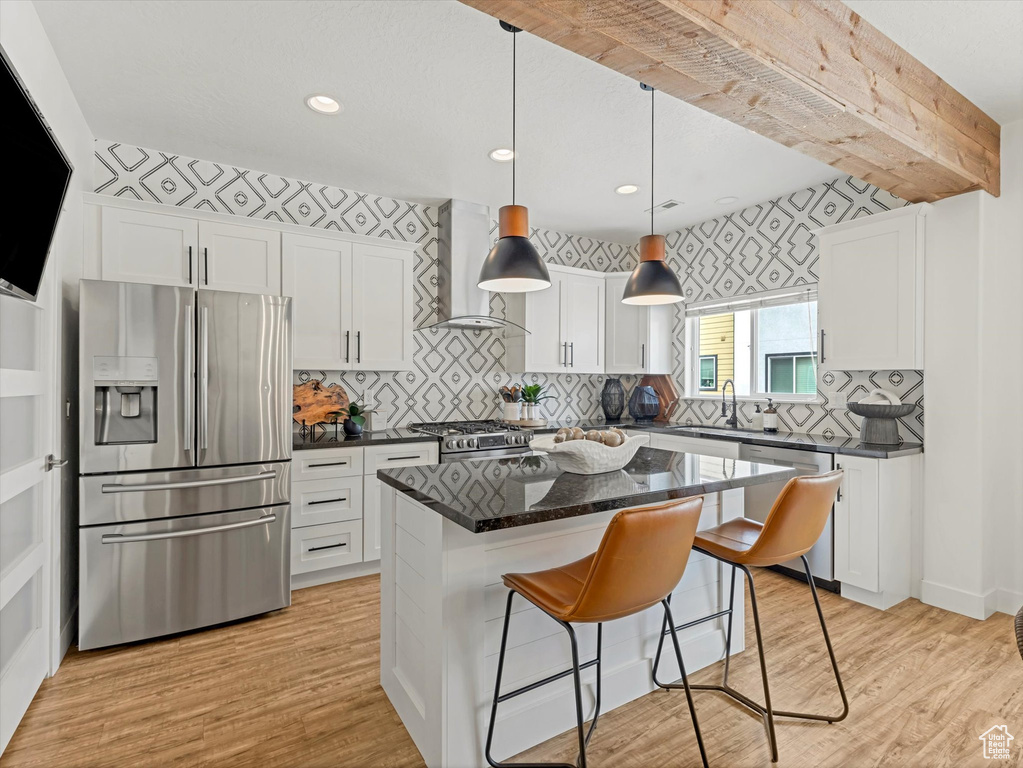 Kitchen with appliances with stainless steel finishes, wall chimney range hood, white cabinets, light wood finished floors, and recessed lighting
